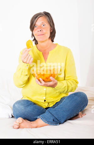 Donna seduta nel letto mangiare patatine Foto Stock