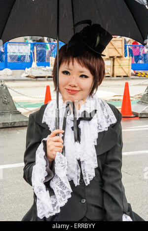 Harajuku, Toyko. Giovane donna giapponese vestita con il classico abito da cameriera in stile "Sweet Lolita" in stile vittoriano e con ombrello nero, sorridente. Foto Stock