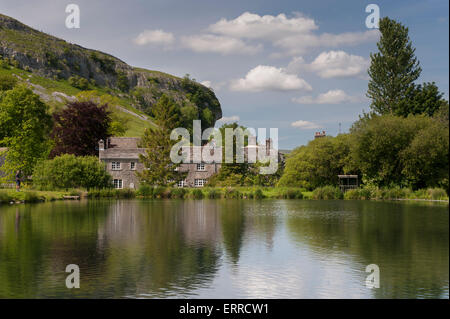 La luce del sole estivo & pittoreschi cottage in pietra stand sulle rive di un suggestivo lago di pesca, Kilnsey Crag oltre - Kilnsey Park, Yorkshire Dales, Inghilterra, Regno Unito. Foto Stock