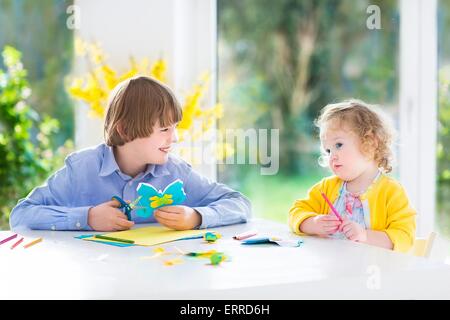 I due ragazzi, felice ragazzo adolescente e sua sorella toddler, divertirsi insieme di disegno, pittura, taglio carta colorate farfalle Foto Stock