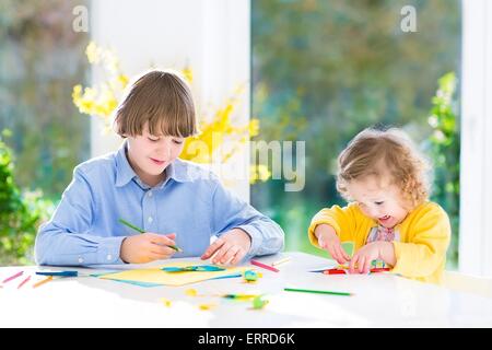 I due ragazzi, felice ragazzo adolescente e sua sorella toddler, divertirsi insieme di disegno, pittura, taglio carta colorate farfalle Foto Stock