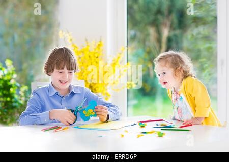 I due ragazzi, felice ragazzo adolescente e sua sorella toddler, divertirsi insieme di disegno, pittura, taglio carta colorate farfalle Foto Stock