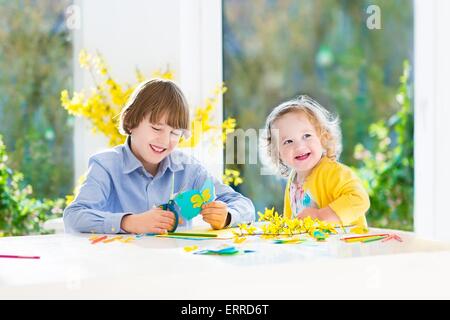 I due ragazzi, felice ragazzo adolescente e sua sorella toddler, divertirsi insieme il disegno, la pittura e il taglio della carta colorata butterfly Foto Stock