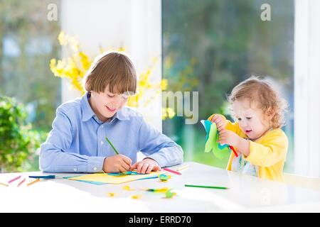 I due ragazzi, ragazzo adolescente e il suo simpatico bimbo sorella, divertirsi insieme il disegno, la pittura e il taglio della carta colorate farfalle Foto Stock