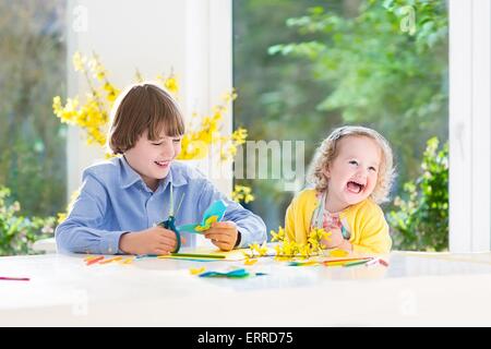 I due ragazzi, felice ragazzo adolescente e sua sorella toddler, divertirsi insieme di disegno, pittura, taglio carta colorate farfalle Foto Stock