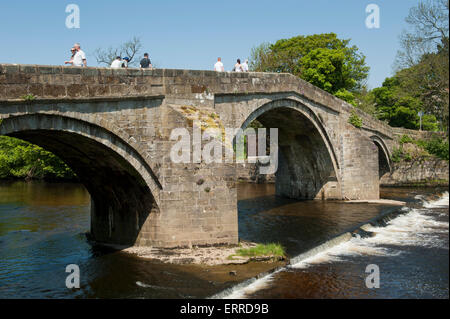 Le persone che attraversano le SCENIC RIVER Wharfe sulla antica pietra packhorse bridge sul flusso di acqua e piccole weir - Ponte Vecchio, Ilkley, West Yorkshire, Inghilterra, Regno Unito. Foto Stock