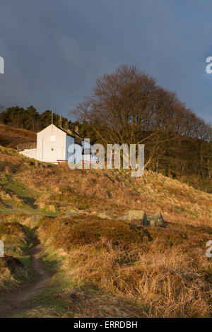 Nel sole sotto un cielo blu, solitaria e isolata, pozzetti bianchi Spa Cottage, è arroccato su un pendio - Ilkley Moor, West Yorkshire, Inghilterra, Regno Unito. Foto Stock