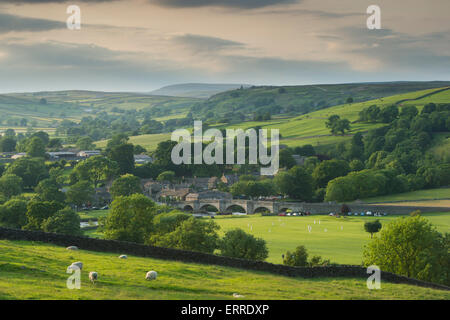 Idillio rurale - bella campagna panoramica collinare e tradizionale villaggio cricket match sulla soleggiata estate sera - Burnsall, Yorkshire Dales, Inghilterra, Regno Unito. Foto Stock