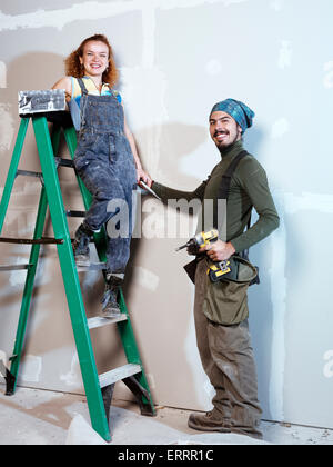 Ritratto di un sorridente coppia giovane rinnovando, installazione di patch su muro a secco Foto Stock