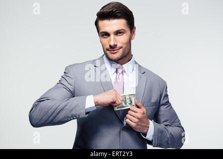 Imprenditore mettere soldi in tasca su sfondo grigio. Guardando la fotocamera Foto Stock