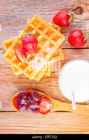 Waffles fatti in casa con confettura di fragole e vetro con latte su sfondo di legno Foto Stock