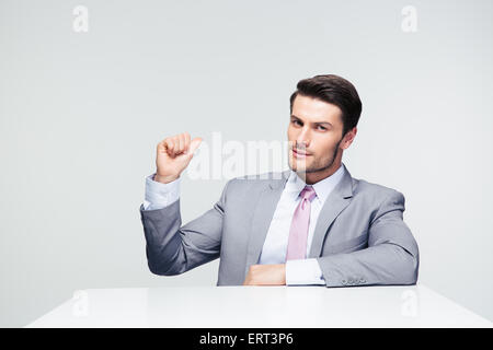 Imprenditore fiducioso seduta al tavolo puntare il dito torna su sfondo grigio Foto Stock