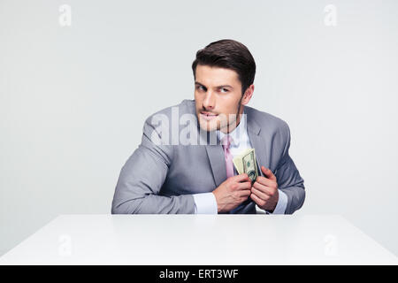 Imprenditore mettere soldi in tasca su sfondo grigio e guardando lontano Foto Stock