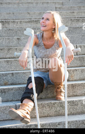 Donna bionda con le stampelle seduti sulle scale Foto Stock