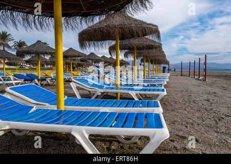 Vuoto azzurro sedie a sdraio sulla spiaggia con ombrelloni di paglia Foto Stock
