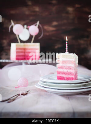 Pezzo di torta di compleanno in rosa e bianco con candela di compleanno su di esso. Foto Stock