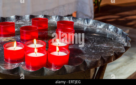 Red candele votive disposti su nero antico candeliere di ferro, alcuni brucia ancora Foto Stock