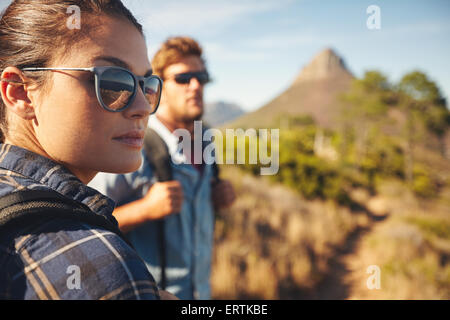 Chiudere l immagine della giovane donna che indossa gli occhiali da sole che guarda lontano con il giovane uomo in background. Coppia caucasica escursionismo in countrysi Foto Stock