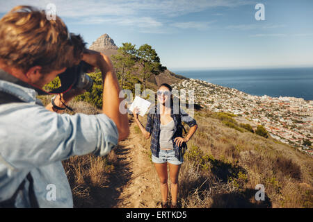 Giovane uomo di scattare le foto della bella ragazza che mostra una mappa in campagna durante il trekking durante le vacanze estive. Coppia giovane hi Foto Stock