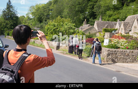 Turisti asiatici a fotografare il XVII secolo cottage in pietra a Bibury, Cotswolds, Gloucestershire, Inghilterra Foto Stock