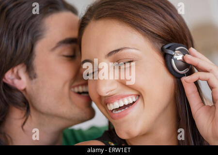 Giovane con le cuffie, uomo whispering in womans orecchio Foto Stock