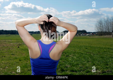 Retro della giovane donna su un campo verde che fissa la sua coda di cavallo Foto Stock