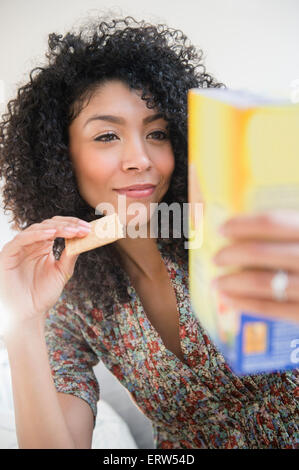 Razza mista donna mangiare cracker e la lettura di informazioni nutrizionali Foto Stock