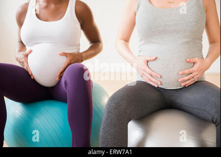 Donne in stato di gravidanza tenendo gli stomaci seduti sulle sfere di fitness Foto Stock