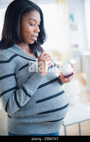 Nero donna incinta di mangiare yogurt Foto Stock