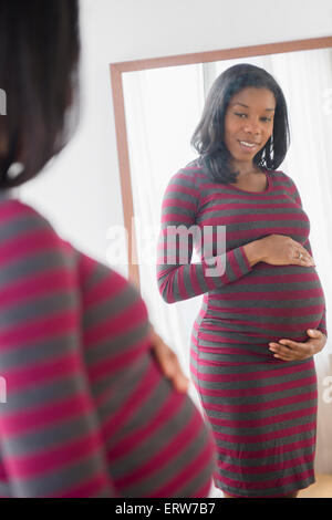 Nero donna incinta ammirando il suo stomaco in specchio Foto Stock
