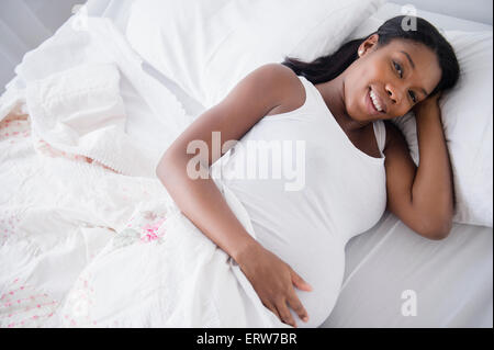 Nero donna incinta sorridente nel letto Foto Stock