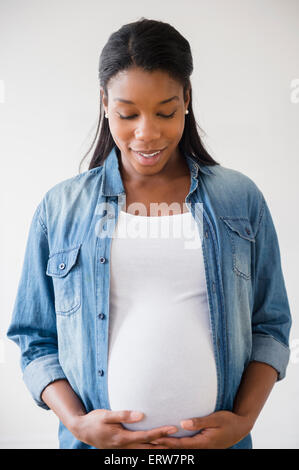Nero donna incinta ammirando il suo stomaco Foto Stock