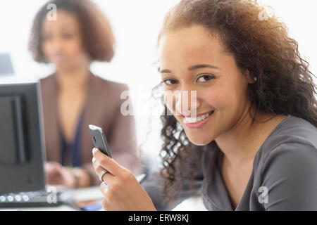 Imprenditrice sorridente con un telefono cellulare in ufficio Foto Stock