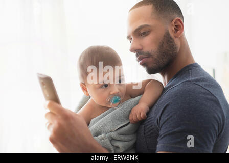 Padre holding baby figlio e utilizzando il telefono cellulare Foto Stock