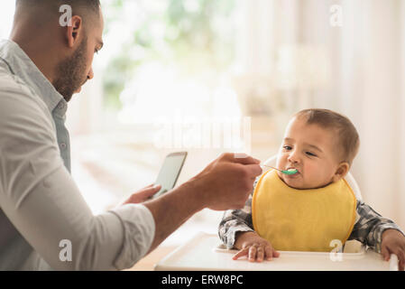 Padre sms sul cellulare e la alimentazione di baby figlio Foto Stock