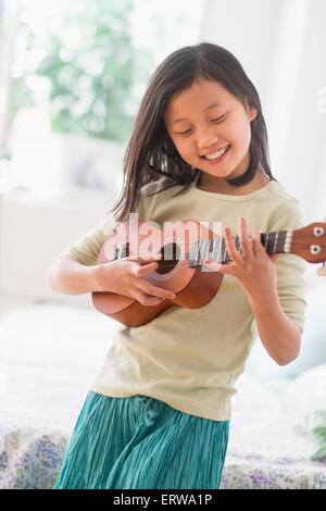 Ragazza cinese la pratica di ukulele in camera da letto Foto Stock