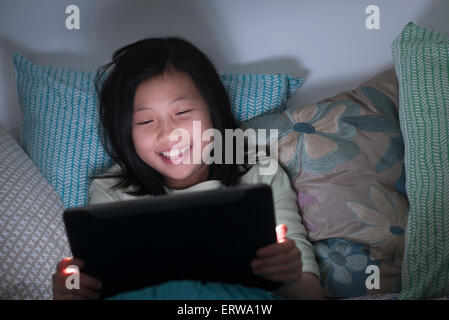 Sorridente ragazza cinese guarda la tavoletta digitale a letto Foto Stock