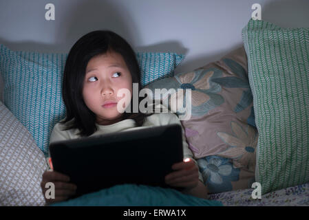 Nervoso ragazza cinese guarda la tavoletta digitale a letto Foto Stock