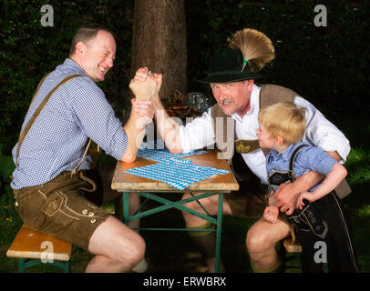 Due uomini bavarese seduta su una panchina e premendo le mani mentre un bambino si erge accanto a loro Foto Stock