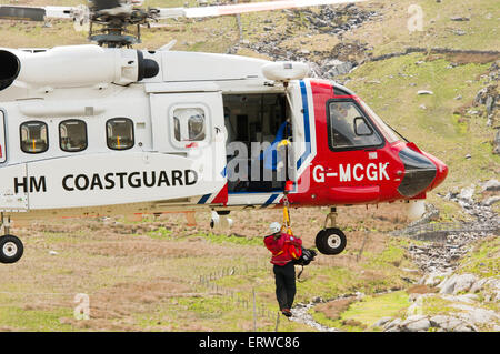 Una montagna soccorritore è winched in un abilmente in bilico Sikorsky S-92 elicottero azionato da Bristow per la Guardia Costiera HM Foto Stock