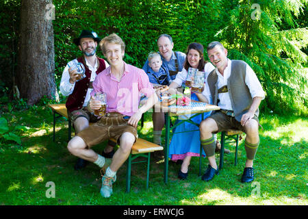 Famiglia bavarese al di fuori seduta su una panchina e bere birra Foto Stock