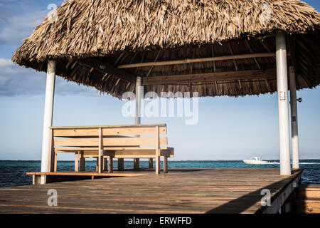 Un sedile dei Caraibi con una vista. Una Palapa banco e alla fine di un dock con vedute dell'oceano sull'isola di Ambergris Caye. Foto Stock