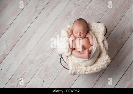 Un ritratto di sette giorni di età, neonato dorme in un cestello in filo metallico su un dipinto di bianco, con pavimento in legno. Foto Stock