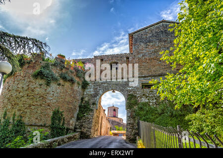 Vista attraverso un antico arco di una torre orologio con pareti in mattoni a guardia di un villaggio di campagna in Italia Foto Stock