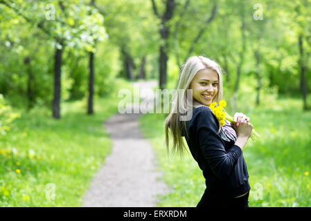 Giovane bella donna con denti di leoni nel parco Foto Stock