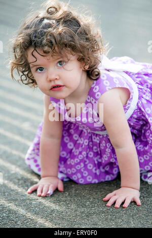 Bambina in abito rosa seduta su strada Foto Stock