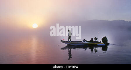 Un bass fisherman pesci per largemouth bass da una barca sul lago a sunrise. Foto Stock