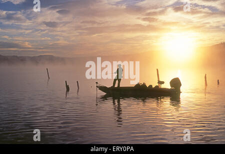 Un bass fisherman pesci per largemouth bass da una barca sul lago a sunrise. Foto Stock