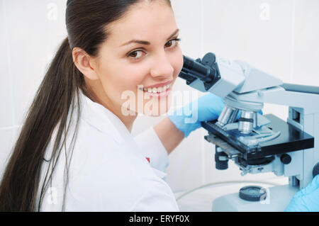 Donna giovane ricercatore medico guardando attraverso il microscopio in laboratorio, il concetto di medicina Foto Stock