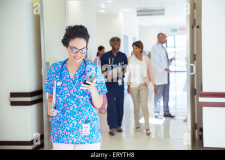 Un infermiere gli sms sul cellulare in ospedale corridoio Foto Stock